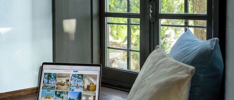 Una computadora portátil sobre un banco de madera junto a una ventana con vista a follaje.