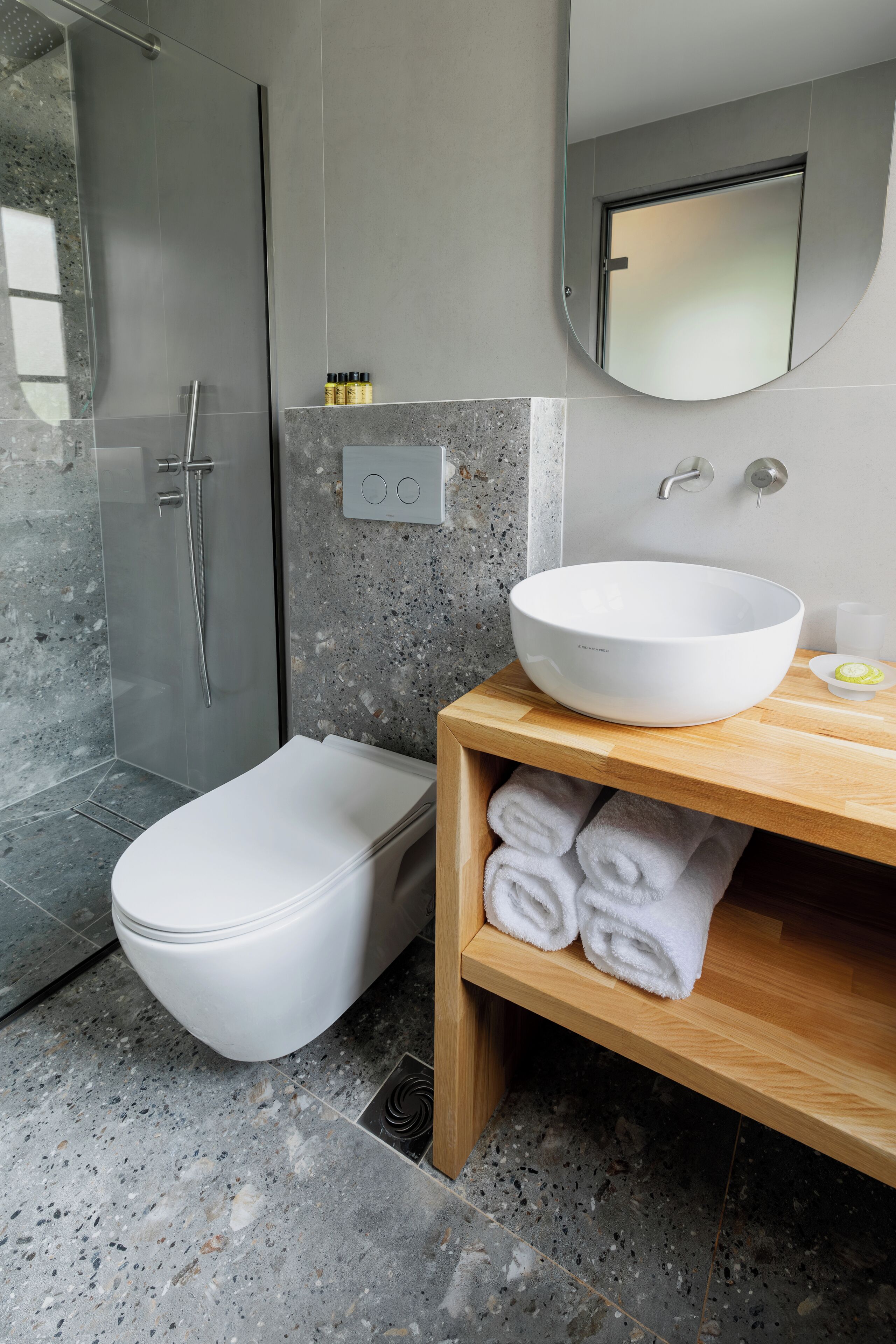 A modern bathroom with a glass-enclosed shower, a white toilet, a wooden vanity with a large white basin, and neatly folded towels.
