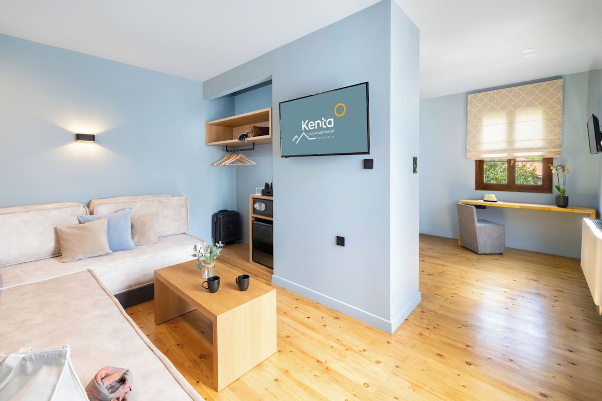 A modern hotel room with a sofa, wooden coffee table, and a TV displaying the hotel name.