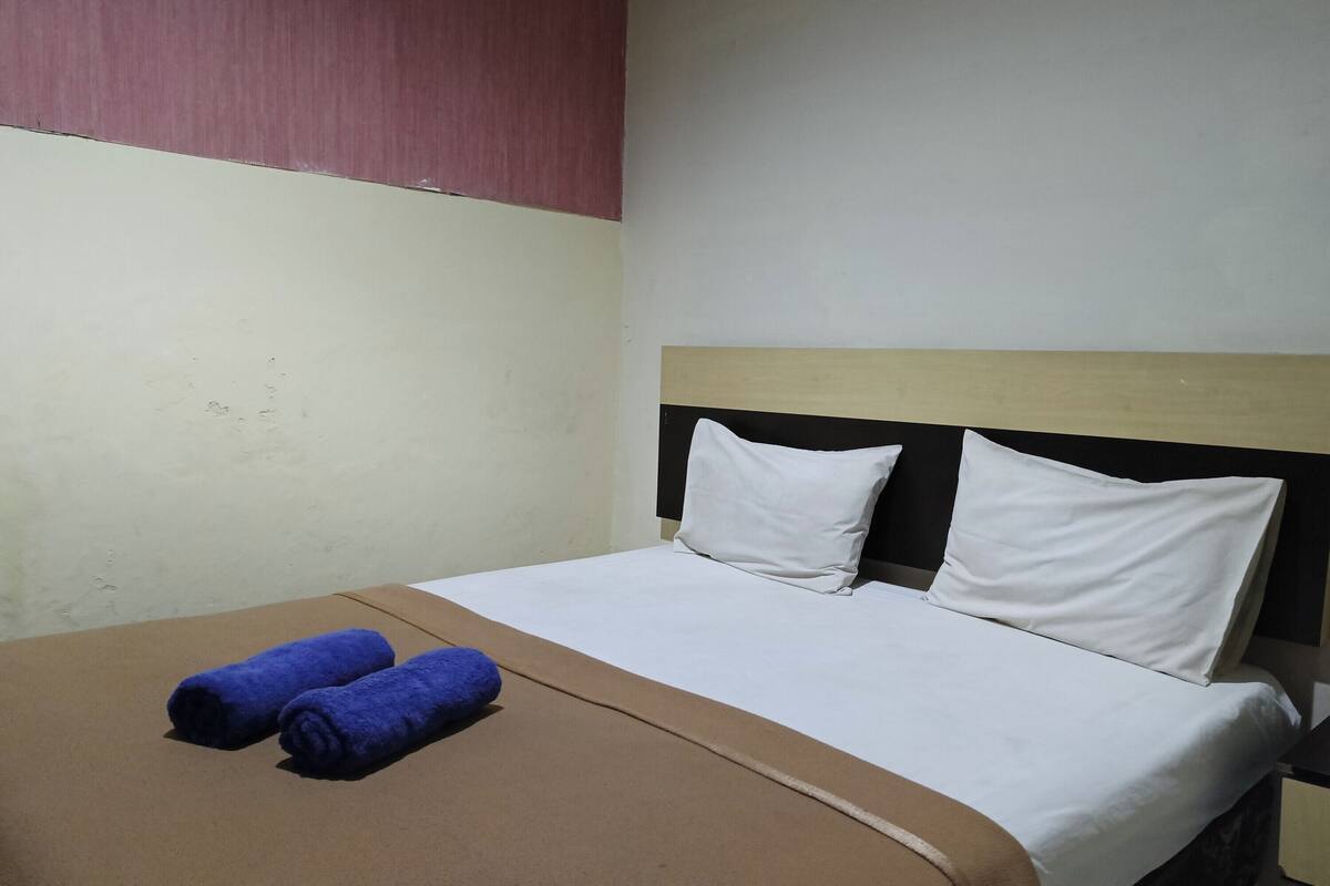 A hotel room with a bed, two pillows, and two rolled towels.