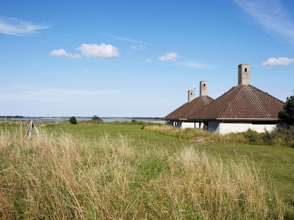 A building with a tiled roof and chimneys, surrounded by grass and a clear sky.