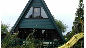 Un bâtiment triangulaire avec un toit végétalisé et un toboggan jaune à l’avant.