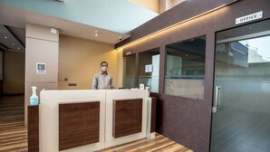 Un mostrador de recepción con un cartel que indica una oficina, un dispensador de gel hidroalcohólico y una puerta de cristal que da a un espacio de oficina.