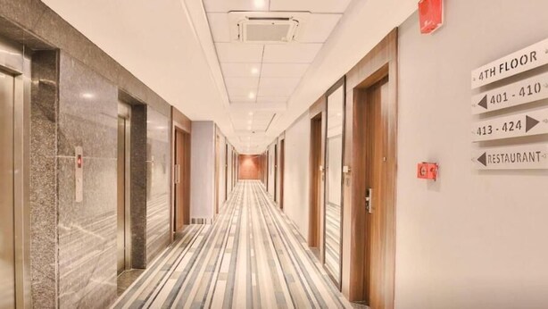 Un pasillo de hotel con piso de mármol, ascensores y señales indicando el cuarto piso, el restaurante y los números de habitación 401-410 y 413-424.