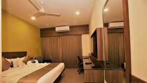 Una habitación de hotel con cama, escritorio, computadora, aire acondicionado y ventilador de techo.