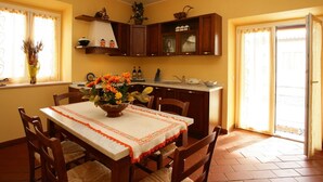 A dining area with a table set for four, a kitchen with wooden cabinets, and a window with curtains. - Villa With Private Pool in Piancastagnaio (Piancastagnaio)