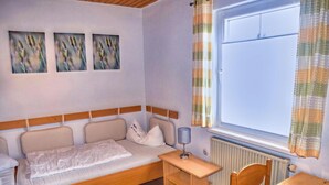 A small, cozy bedroom with a single bed, a wooden nightstand, a table, and a window with curtains. - Peaceful Garden Apartment (Fuessen)