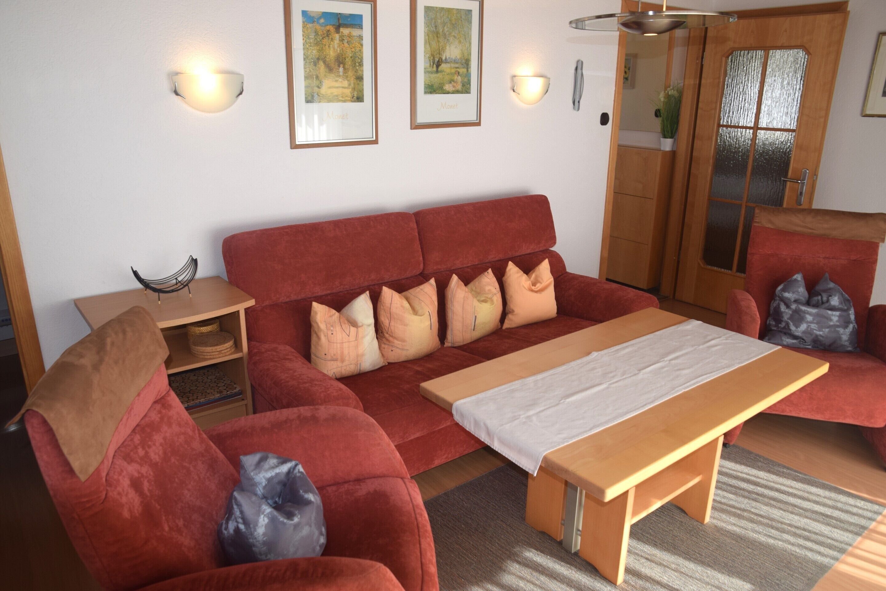 Un canapé rouge, une table en bois, une petite étagère et des lampes fixées au mur.