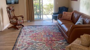 Un salon avec un canapé en cuir marron, un fauteuil à bascule à motifs floraux et un tapis à dessins.