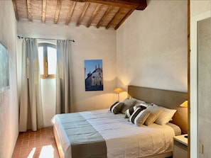 A bedroom with a bed, two bedside lamps, a window with curtains, and a wall-mounted picture. - Holiday Home Casa Lena (Gavorrano)
