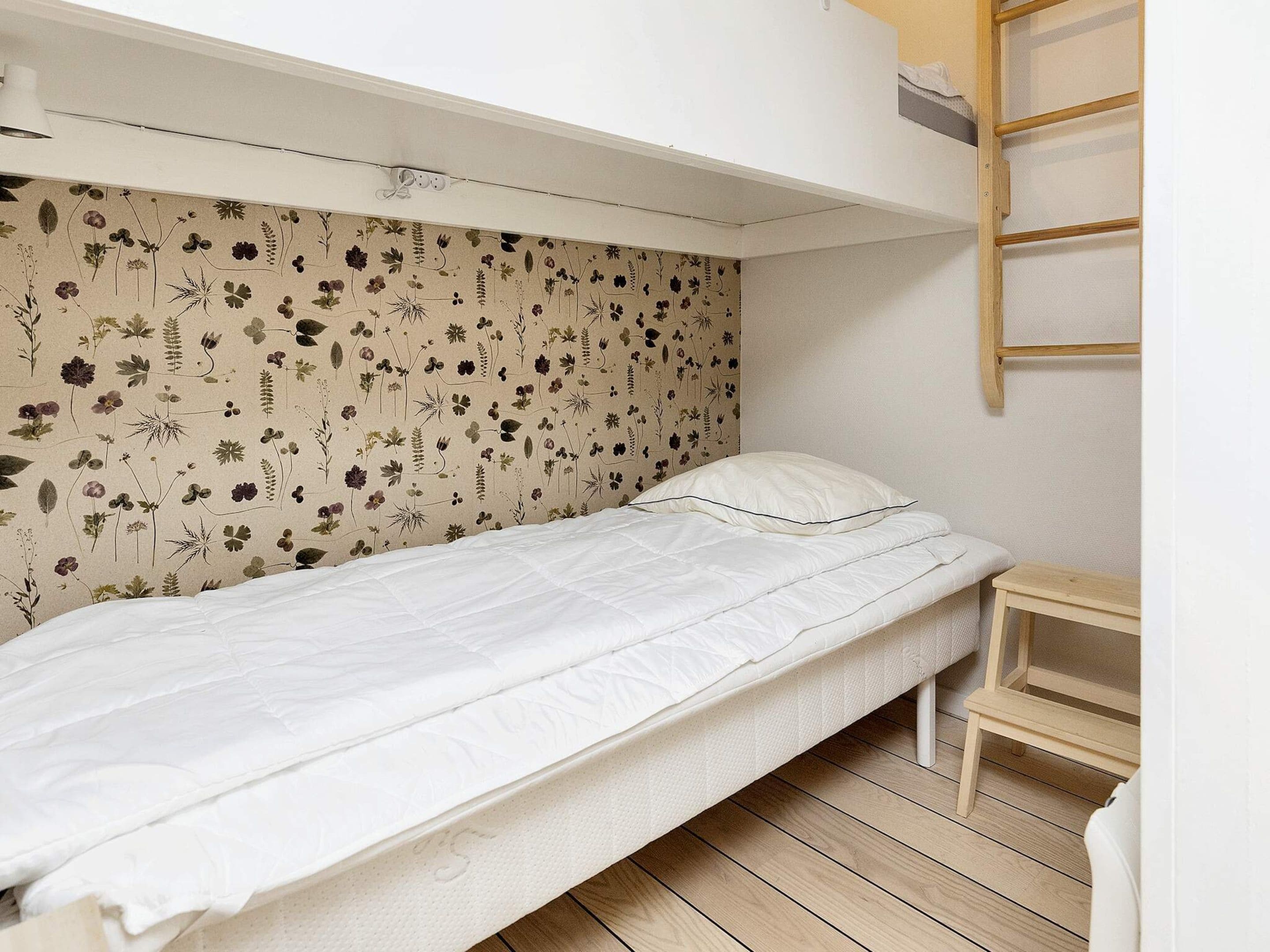 A single bed with a floral-patterned headboard in a small, well-lit room with a wooden floor.