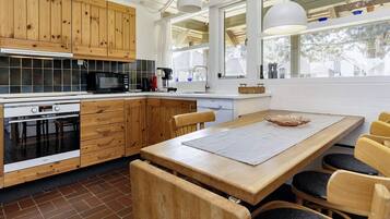 A modern kitchen with wooden cabinets, a built-in oven, and a dining area with a large table and chairs.