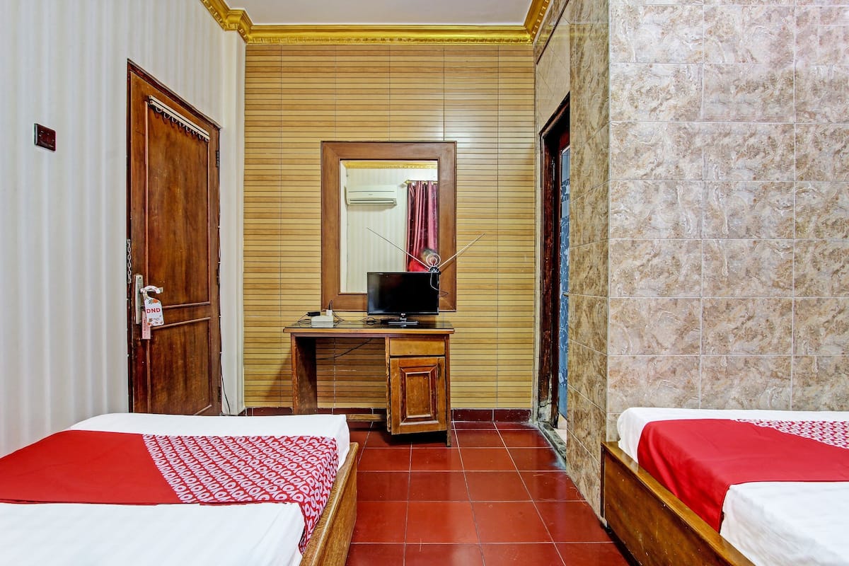 Une chambre d’hôtel avec deux lits, un bureau en bois avec une télévision et un miroir au mur.