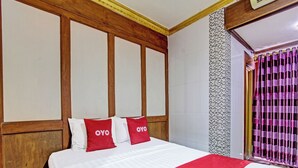 Une chambre d’hôtel avec un grand lit, une tête de lit en bois et une couvre-lit à motifs rouges et blancs.