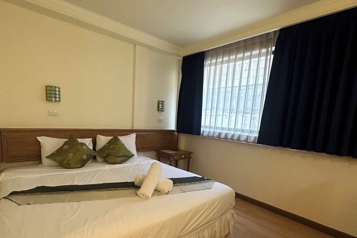 A hotel room with a large bed, a small bedside table, a window with curtains, and a wall-mounted light.