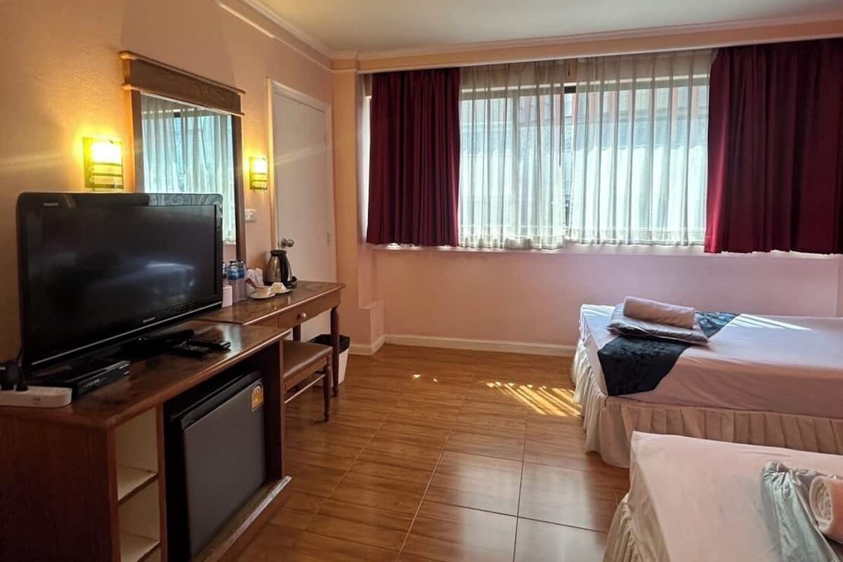 A hotel room with a television, a desk, a chair, a bed, and a window with curtains.