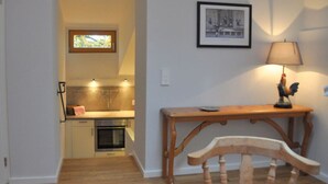 A room with a wooden table, a chair, a lamp, a framed picture, and a kitchen area with a stove and oven. - Suite Nuss Modern Retreat (Bad Wiessee)