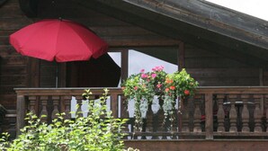 A wooden building with a balcony, a red umbrella, and potted plants with flowers. - Suite Nuss Modern Retreat (Bad Wiessee)