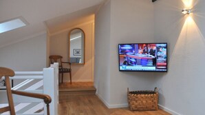A modern living room with a television mounted on the wall, a wooden chair, a wicker basket, and a white table. - Suite Nuss Modern Retreat (Bad Wiessee)