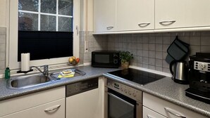 A compact kitchen with a dishwasher, oven, microwave, and a coffee maker. - Maila - Marbi (Varel)