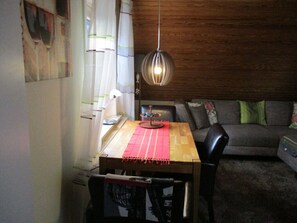 Enjoy meals in this dining area with a wooden table and chairs, a sofa, and a window with white curtains.