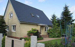 Ein zweistöckiges Haus mit einem dunklen Ziegeldach, beige verkleideten Wänden und einer kleinen Veranda.