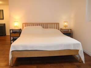 A single bed with a wooden frame and white bedding in a room with wooden flooring. There are two bedside tables with lamps on either side of the bed. - Belvilla by OYO Villetta Carla (Lazise)