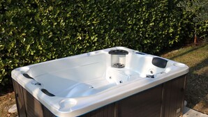Ein rechteckiges Whirlpool mit integriertem Sitzplatz und Bedienfeld, auf einer Steinterrasse im Freien platziert.