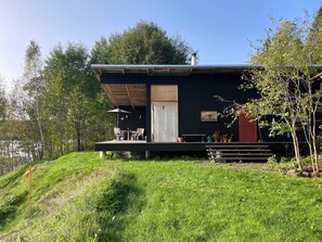 Uma casa moderna com telhado plano, varanda coberta com móveis para área externa e vista para uma área arborizada.