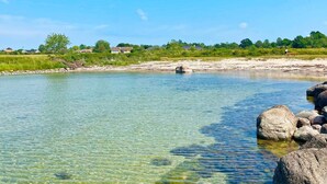Un río cristalino con rocas, un banco y casas al fondo.