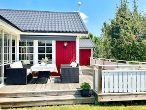 A wooden deck with outdoor furniture, a red door, and a covered area with a table and chairs.