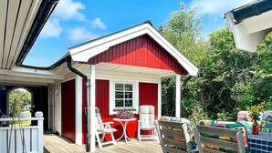 Un espacio al aire libre cubierto de rojo y blanco, con piso de madera, sillas blancas y una pequeña mesa.