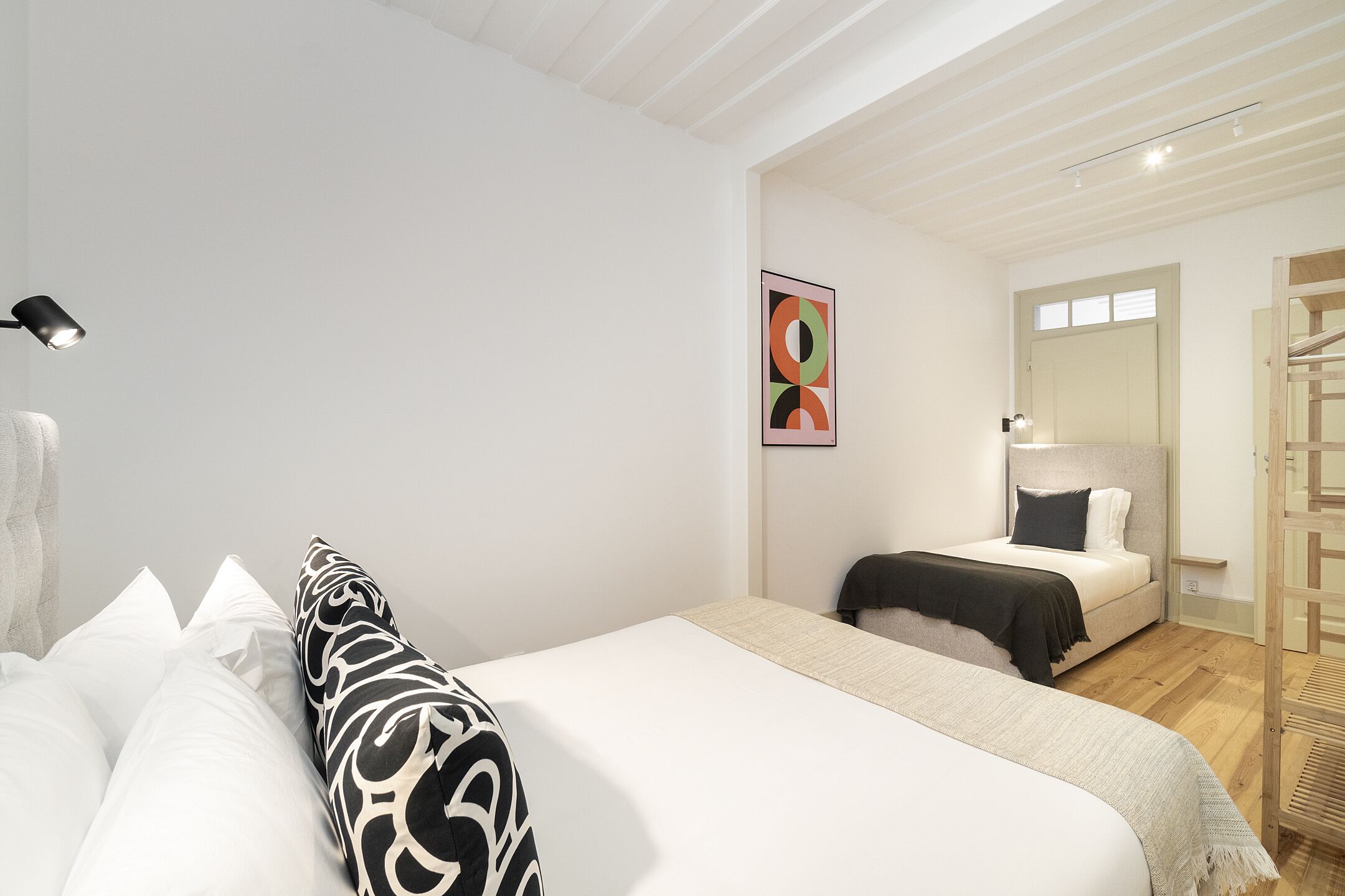 A bedroom with a bed, a bedside table, a lamp, a mirror, and a door leading to another room.