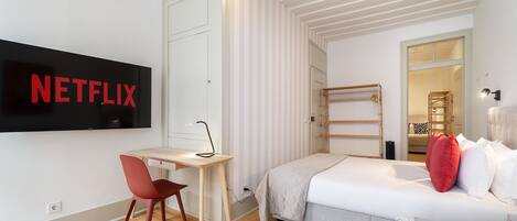 Un dormitorio moderno con cama, escritorio, silla y televisor fijado a la pared.