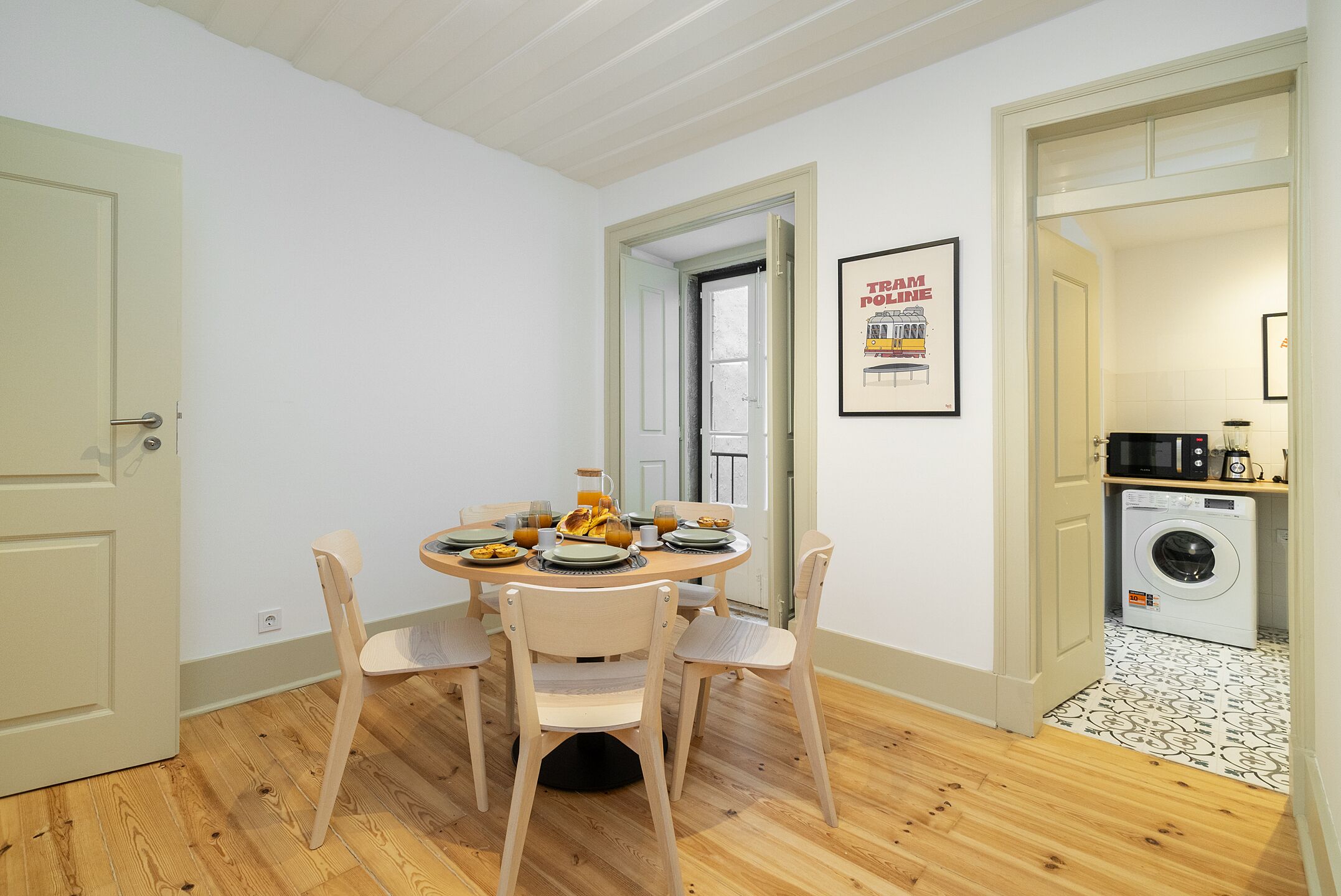 A dining area with a round table, four chairs, and a breakfast setting. There is a washing machine in the background.