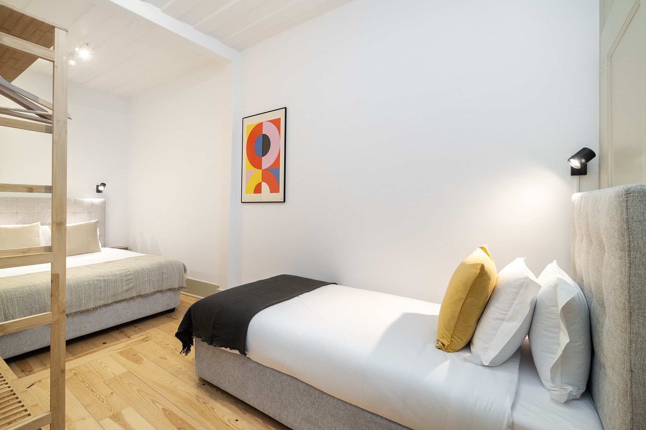 Quarto moderno com uma cama beliche, uma cama de solteiro e um quadro abstrato colorido na parede.