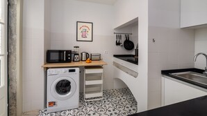 Cocina compacta con lavadora, microondas, tostadora y ollas colgantes.