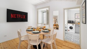 Un comedor con una mesa redonda dispuesta para cuatro personas, un televisor montado en la pared y una lavadora en la habitación contigua.