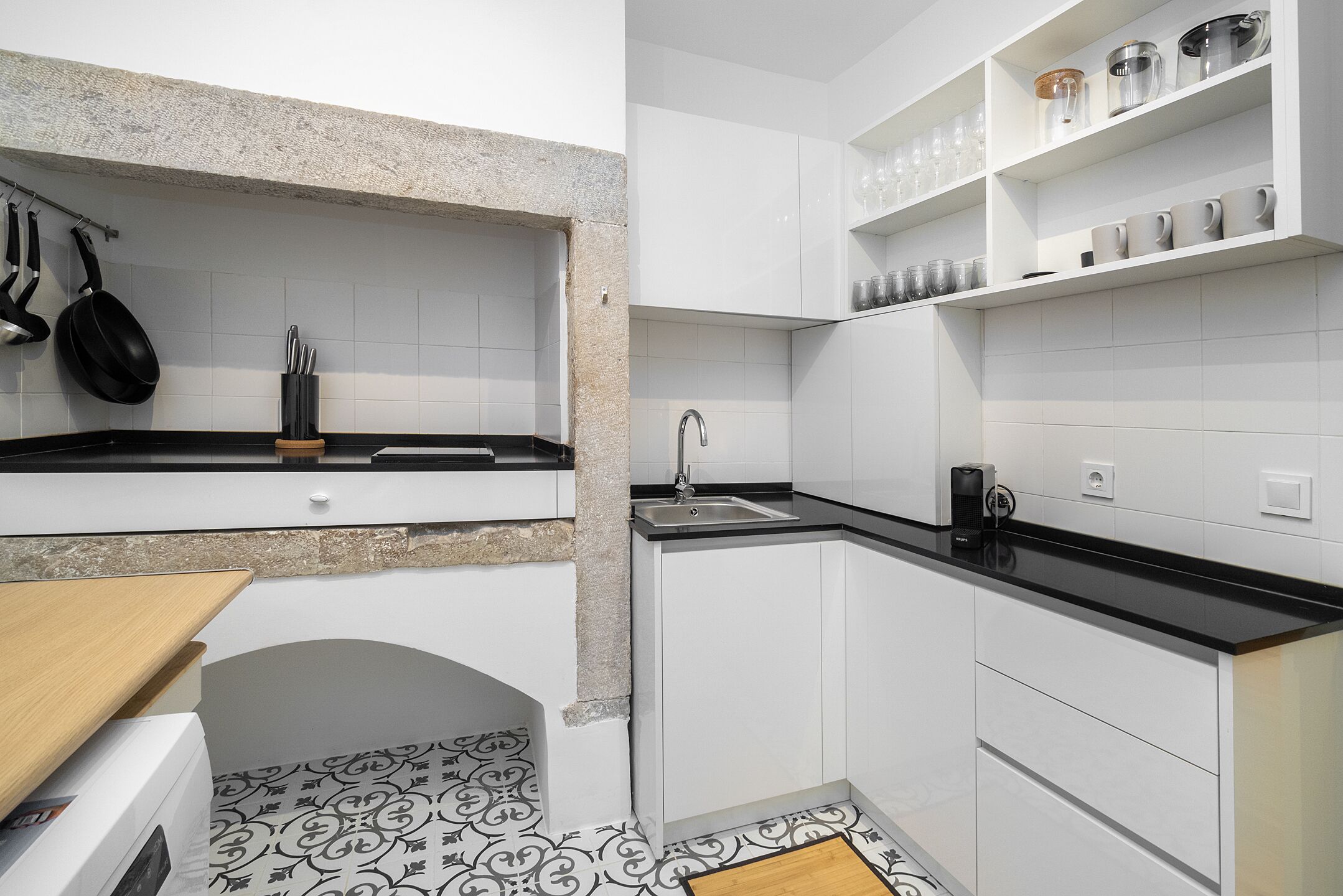 Une cuisine de taille réduite avec des meubles blancs, un plan de travail noir et un carrelage décoratif.