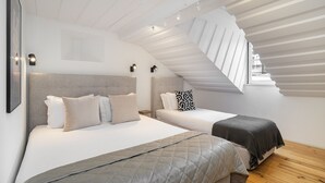 Un dormitorio moderno con dos camas, techo inclinado y tragaluz.