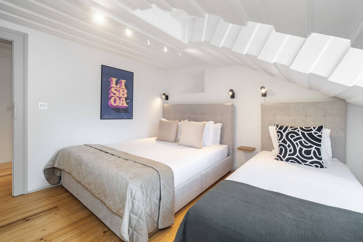 Une chambre avec deux lits, un luminaire au plafond et une œuvre d’art accrochée au mur.