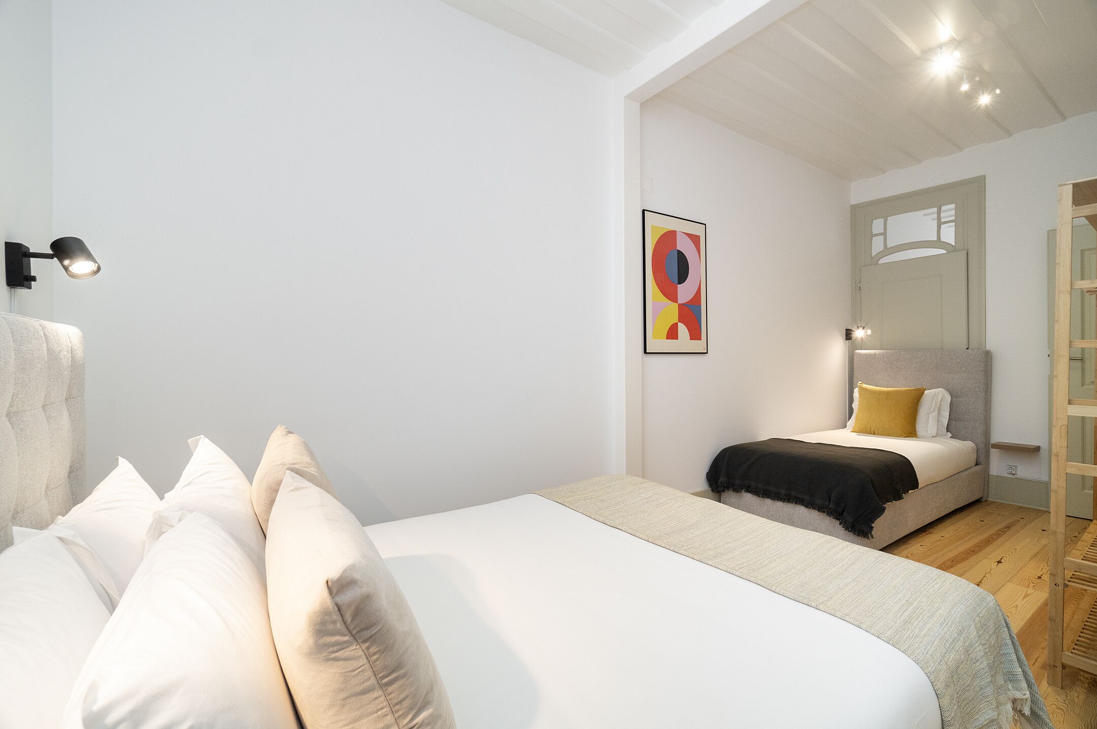 Un dormitorio con una cama grande, una cama más pequeña, una obra de arte en la pared y una escalera de madera.