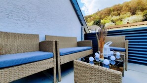 Un espace de détente extérieur aménagé avec des meubles en osier, des coussins, une lanterne et des guirlandes lumineuses décoratives.
