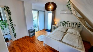 Une chambre à coucher avec un lit, une table de chevet, un luminaire suspendu et une vue sur un balcon.