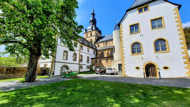 Un bâtiment historique doté d’une tour imposante, d’une cour avec un arbre et d’un chemin pavé.