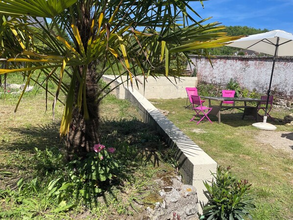 A garden area with a concrete planter, a palm tree, and pink chairs under a white umbrella.