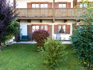 A two-story building with a balcony, a small garden, and a seating area with chairs.