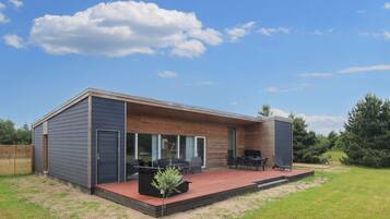 A modern house with a covered patio, a small garden, and a wooden deck.