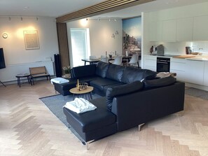 A modern living room with a black leather sofa, a round coffee table, and a dining area with a white table and chairs. - 4 Star Holiday Home in Vaeggerlose (Vaeggerlose)