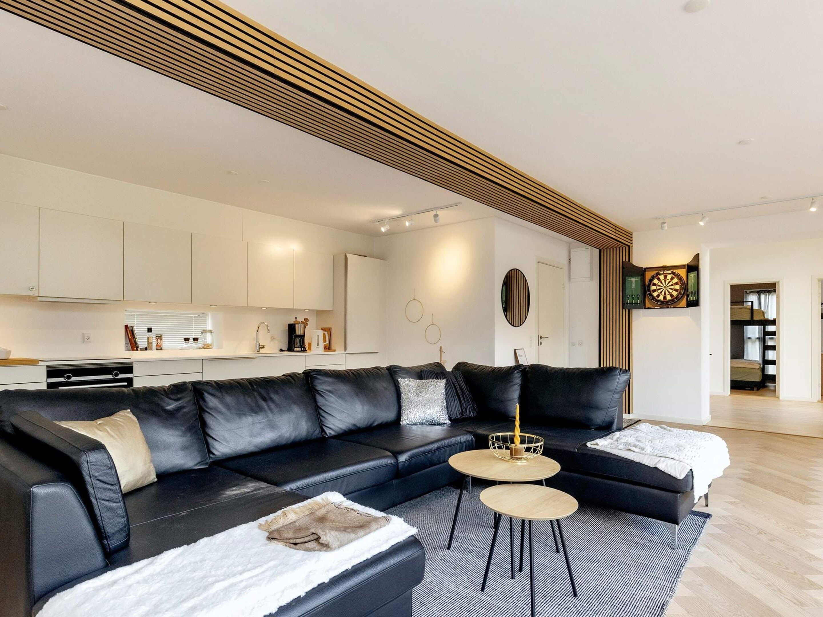 A modern living room with a black leather sectional sofa, two round coffee tables, and a white rug.